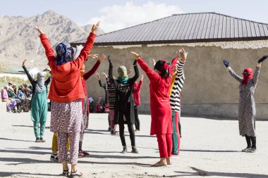 Murghab, Tajikistan, August 23 2018: Kyrgyz girls and young women are practicing a dance on the playground of a school in Murghab. Against the strong sunlight they have protected their faces with scarves. clipart