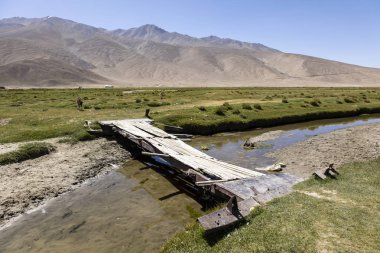 Aged bridge over a small river in Bulunkul in the Pamir mountains in Tajikistan clipart