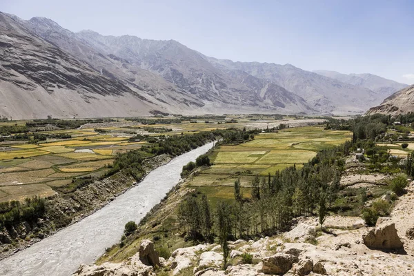 Vruchtbare per dal met de Pandzj rivier in de buurt van Vrang in Tadzjikistan. De bergen op de achtergrond zijn de Hindu Kush in Afghanistan — Stockfoto