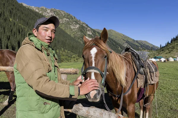 Altyn-Arashan, Kyrgyzstán, 14 srpna 2018: Mladý Kyrgyzština láskyplně hladí koně v údolí Altyn-Arashan v Kyrgyzstánu — Stock fotografie