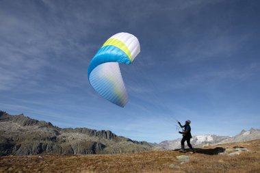 Young paraglider pilot exercises with his paraglider pulling up in the wind, the so-called ground handling. Near Grimsel in the Swiss Alps clipart