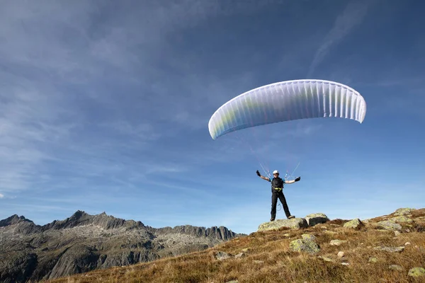 Параплана-пілот стоїть на скелі і балансує його параплана над головою біля озера Грімсель у швейцарських Альпах — стокове фото