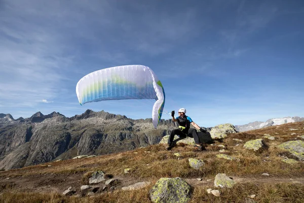 Piloto de parapente se sienta en una roca y equilibra su parapente por encima de su cabeza cerca del lago Grimsel en los Alpes suizos —  Fotos de Stock