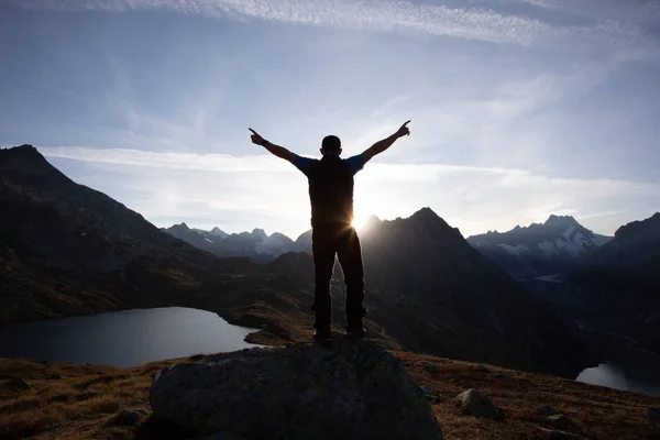 Hiker is standing on a rock with raised hands and enjoying sunrise in the Alps in Switzerland Stock Picture