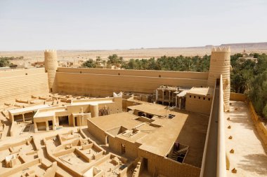 Raghba, Suudi Arabistan, 16 Şubat 2020: Raghba Suudi Arabistan 'daki şatonun köşe kulesine sahip kale duvarının görüntüsü. İnşaat işçileri tadilatta. Kale güzel bir şekilde bir hurma koruluğunun ortasına yerleştirilmiş..