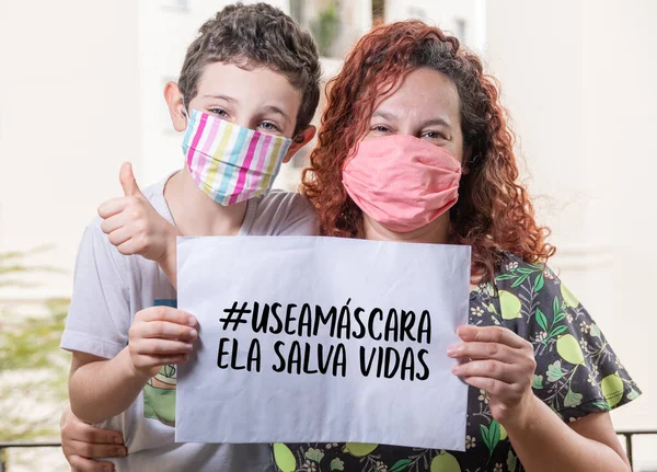 Brazilian mom and son wearing mask holding  paper written: (wear the mask, it saves lives) - Selective Focus
