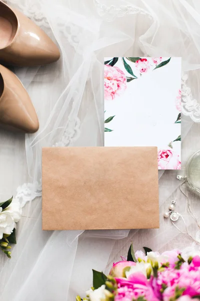 Davetiyeler düğün kağıtları masaya döşeme çiçekler, vual, yüksek topuklu ayakkabılar ve bir şişe tuvalet suyu ile süsleyin. Mockup boş kartpostal ile 