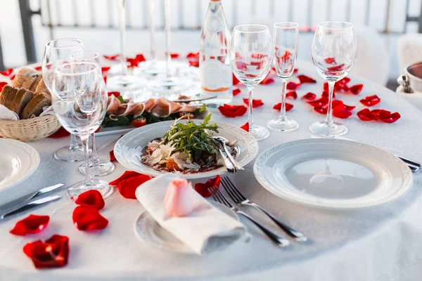 Romantik Sevgililer günü akşam yemeği ayarda gül yaprakları ve boş kadehlerin günbatımı