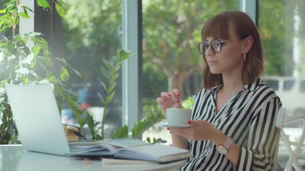 Meisje in een zwart-wit gestreepte blouse met een laptop in een lichte kamer — Stockvideo