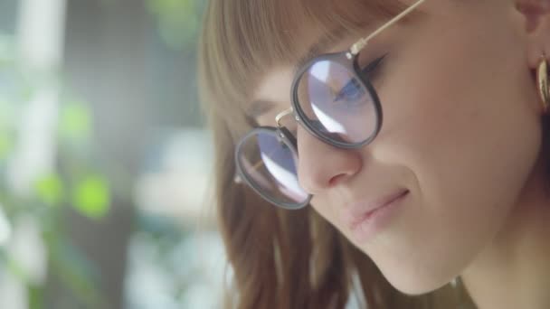 O rosto de uma linda garota morena com óculos: ela lê notas — Vídeo de Stock