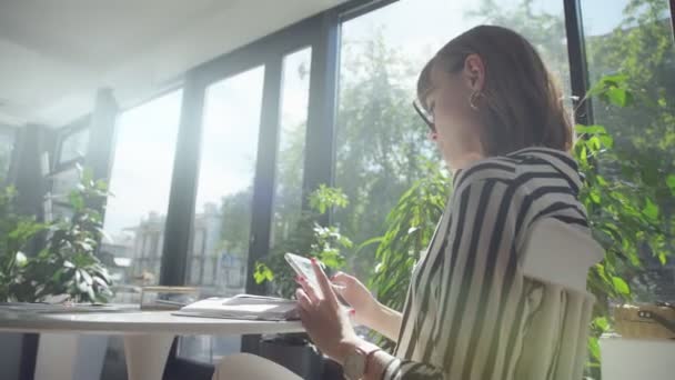 Mujer morena sola en la cafetería con ventanas panorámicas, usando teléfono inteligente — Vídeos de Stock