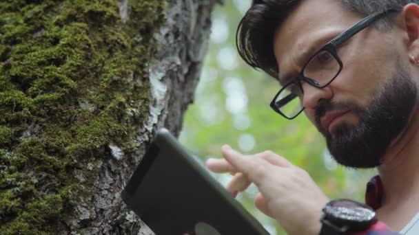 Ekolog studier mossa på ett träd och skriver data till en surfplatta. — Stockvideo