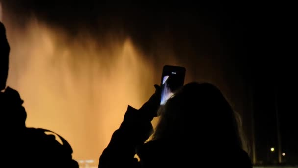 A female tourist takes on the phone a show of dancing fountains. Color water show — Stock Video