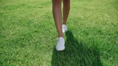 Kadın beyaz spor ayakkabı ayaklarda parlak yeşil çim yürüyor