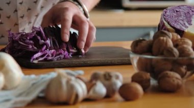 Adam güvenle koyu ahşap kesme tahtası üzerinde kırmızı lahana salatası için dilimler. Çevre sarımsak ve fındık. Mens bilezik ve pişirme sürecinde aksesuarlar eller. Yakın çekim: kesme tahtası ve ürünleri.