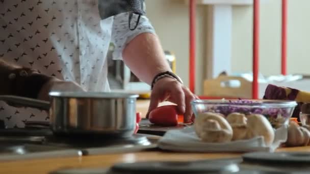 Man cuts red pepper, standing in front of the kitchen table. — Stock Video