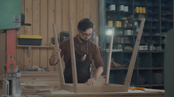 Carpinteiro moderno em oficina conecta as pernas de um produto de madeira . — Vídeo de Stock