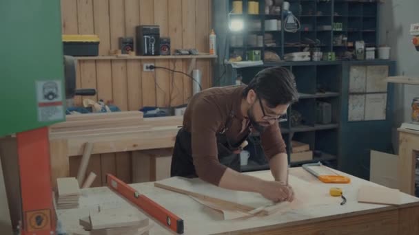 Timmerman met een bril en een baard maakt aantekeningen op de houten balk. — Stockvideo