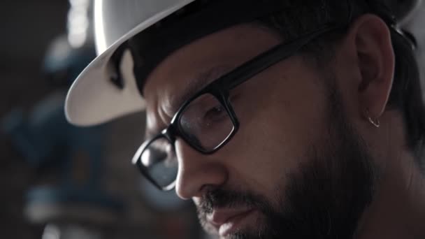 Профиль человека в шлеме, очки: он смотрит вниз на лист с записками — стоковое видео