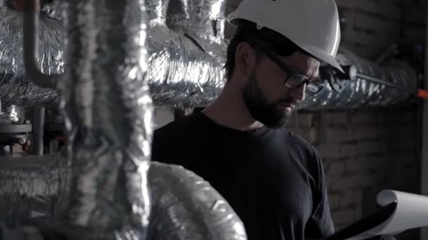 Ingeniero o técnico trabaja en sala de calderas cerca de tuberías, toma notas — Vídeos de Stock