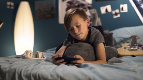 Junge spielt Smartphone im Bett — Stockvideo