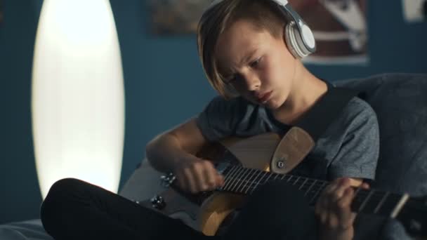 Pojke i hörlurar lärande låt med gitarr — Stockvideo