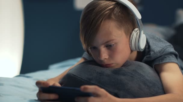 Junge spielt Smartphone im Bett — Stockvideo