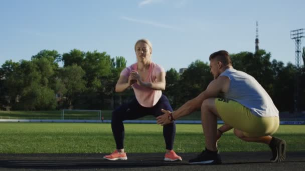 Allenatore aiutare la donna con squat sul campo — Video Stock