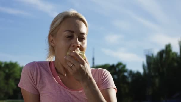 Frau isst Apfel im Sonnenlicht auf Feld — Stockvideo