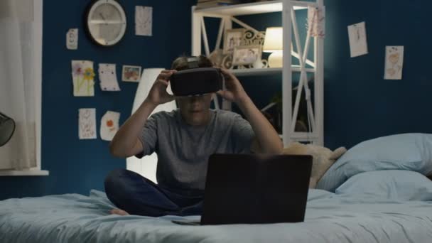 Garçon utilisant des lunettes VR et ordinateur portable sur le lit — Video
