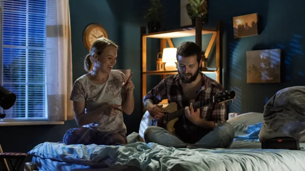 Speelse paar zang met gitaar op bed — Stockfoto