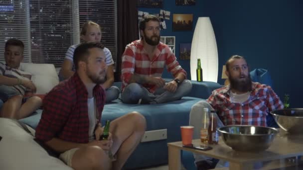 Teman-teman duduk di sofa sambil menonton pertandingan di TV — Stok Video