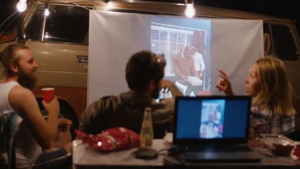 Друзья смотрят видео с проектором в кемпинге — стоковое видео