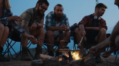 Alacakaranlıkta kamp ateşi üzerinde Sosis kızartma arkadaşlar