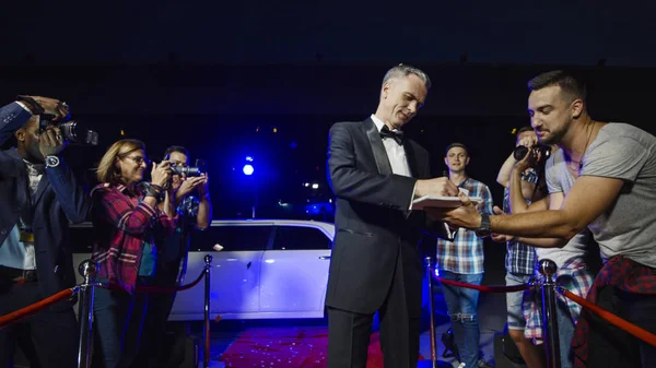 Adult celebrity giving autographs on red carpet