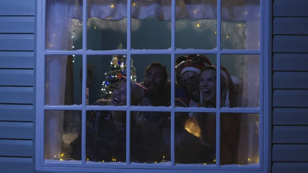 Glada vänner tittar ut i fönstret under julen — Stockfoto