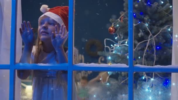 Charming girl through window in Santa hat — Stock Video