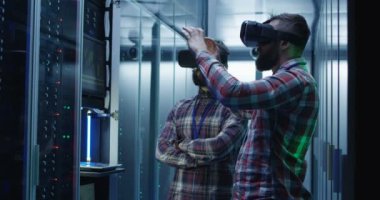 VR kulaklıklar giyen ve veri merkezindeki sunucu raflarla koridorda coworking yetişkin sakallı erkekler