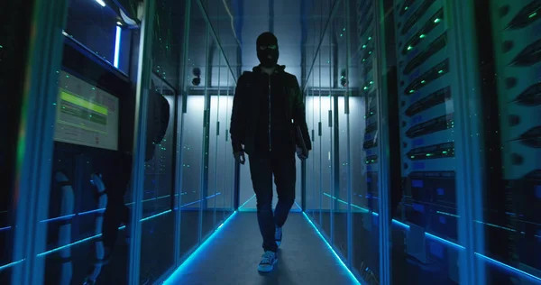Masked hacker walking through rows of servers