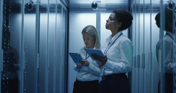 Dos mujeres están trabajando en un centro de datos con filas de bastidores de servidores — Foto de Stock