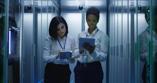 Dos mujeres están trabajando en un centro de datos con filas de bastidores de servidores — Foto de Stock