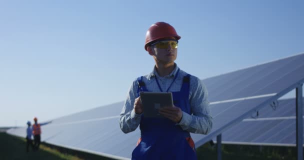 Trabalhador étnico em chapéu duro usando tablet entre painéis solares — Vídeo de Stock