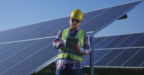 Adult engineer using tablet working among solar panels — Stock Video