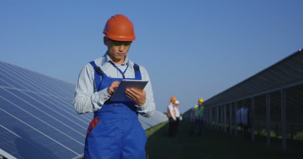 Trabajador étnico en hardhat usando tableta entre paneles solares — Vídeo de stock