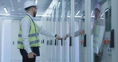 Elektrik İstasyonu mühendis yelek ve kask bir raf yürür ve kapıyı açar ve belgeleri alır.