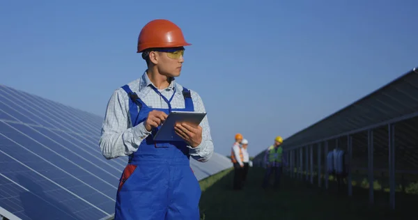 Etnicznych pracownika w kasków ochronnych przy użyciu tabletu wśród paneli słonecznych — Zdjęcie stockowe