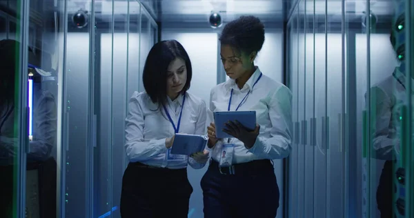 Dos mujeres están trabajando en un centro de datos con filas de bastidores de servidores — Foto de Stock