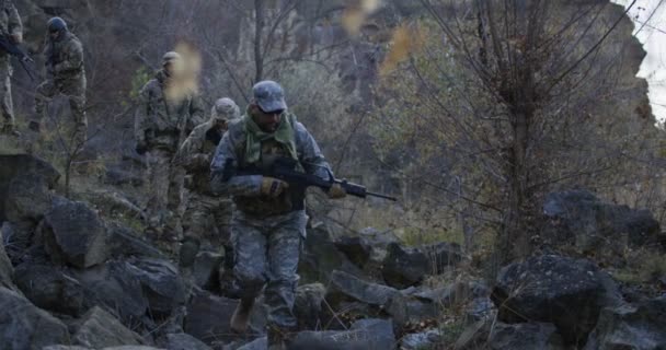 Tentara bersenjata berjalan melalui batu di senja hari — Stok Video