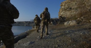 Silahlı askerler bir göl kenarında yürüyüş