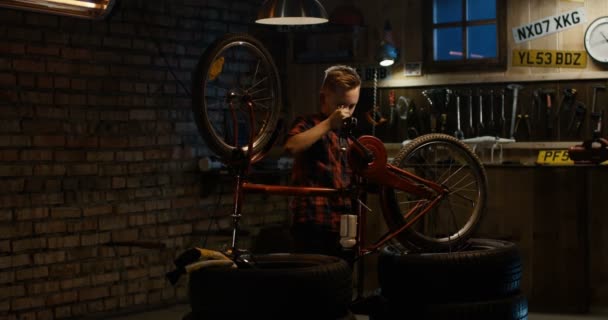 Menino reparando uma bicicleta em uma garagem — Vídeo de Stock